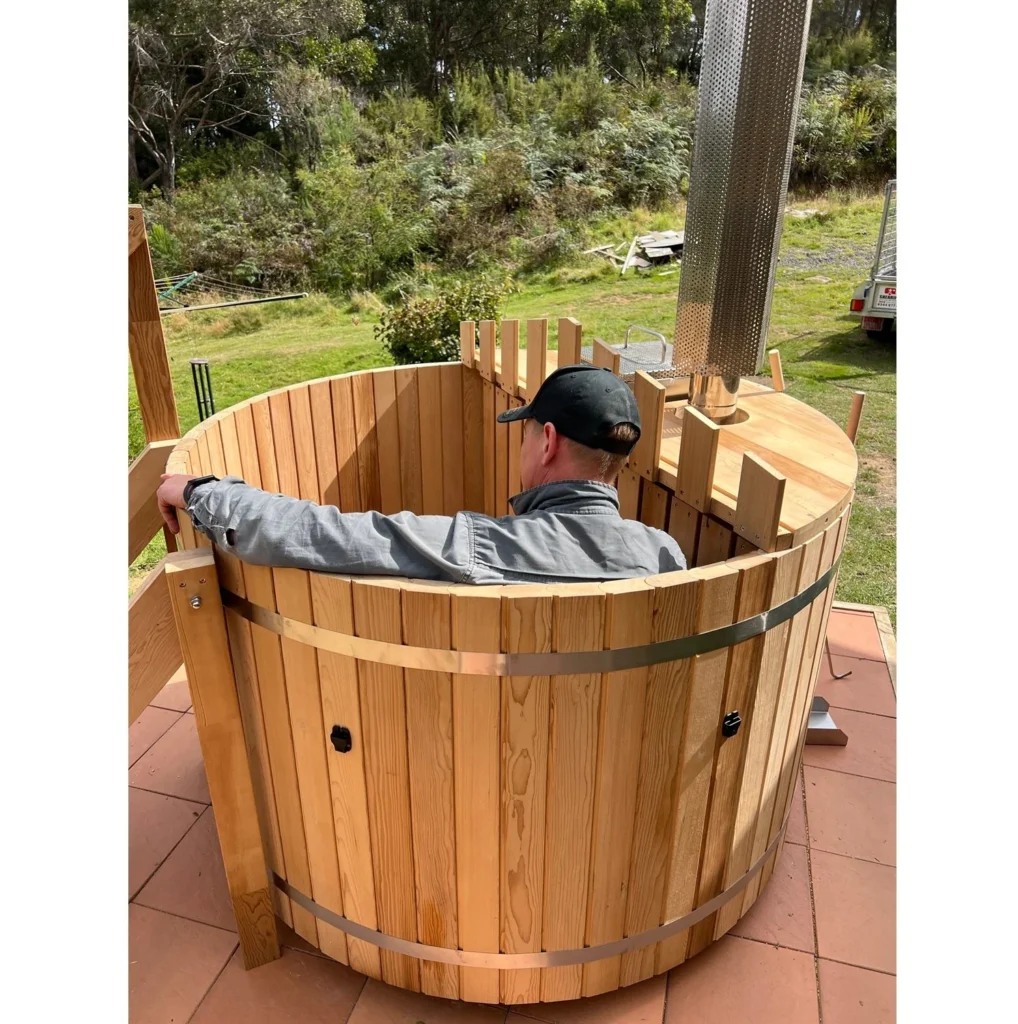 Man sitting in a cedar hot tub heated by an internal wood fired stove