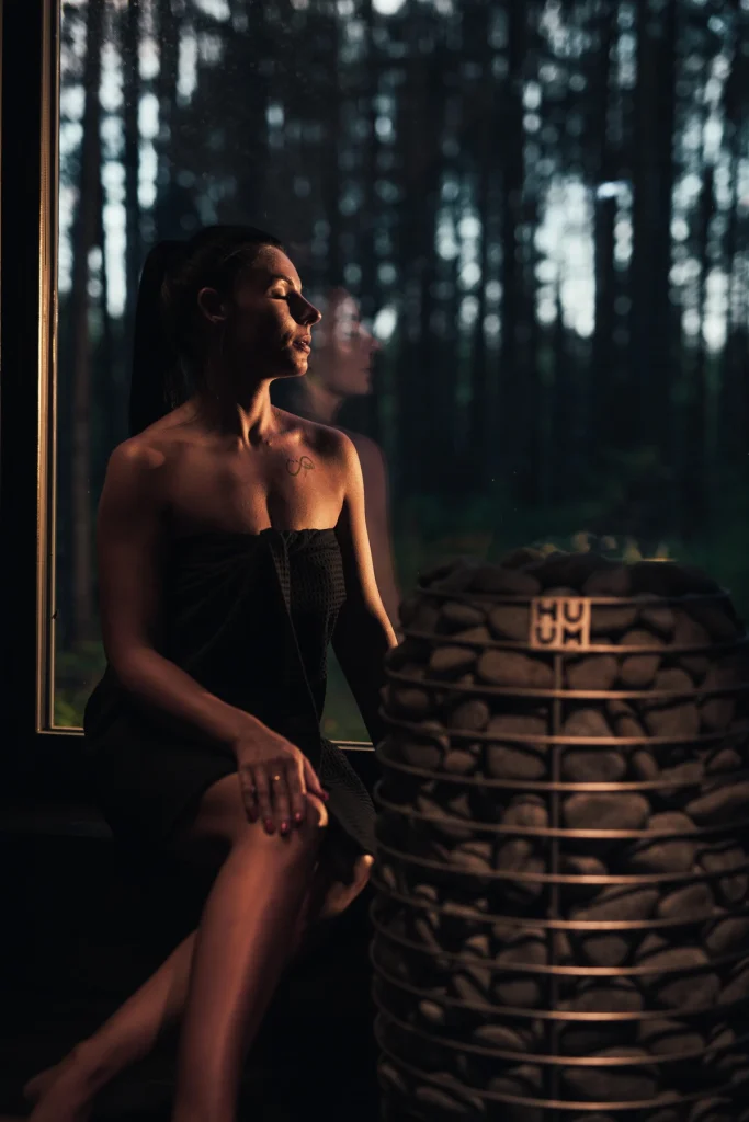 Woman sitting by the sauna window next to the HUUM HIVE Mini heater
