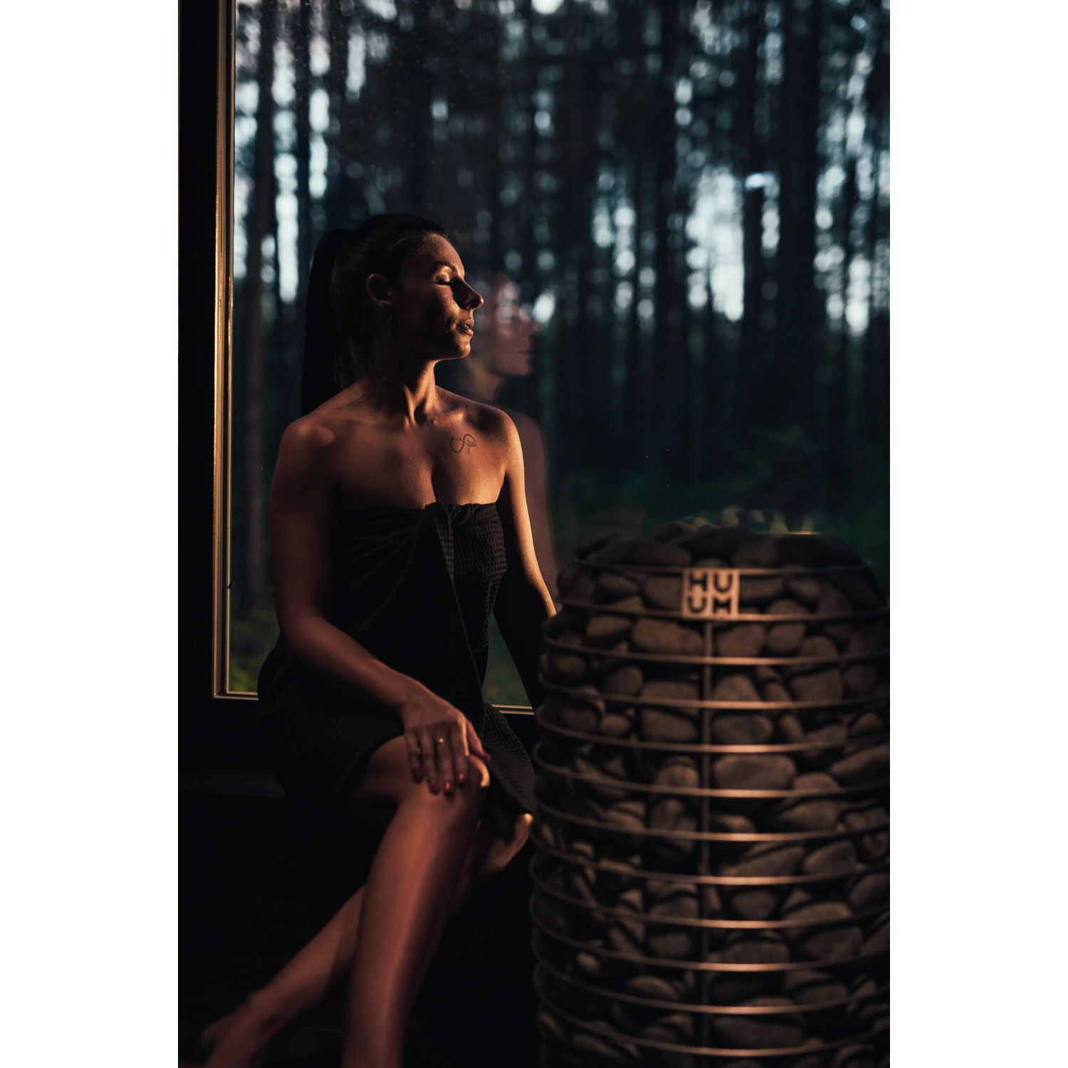 Woman sitting by the sauna window next to the HUUM HIVE Mini heater