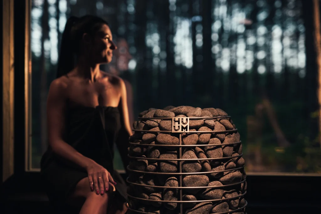 Woman relaxing beside the HUUM HIVE Mini heater in an evening sauna