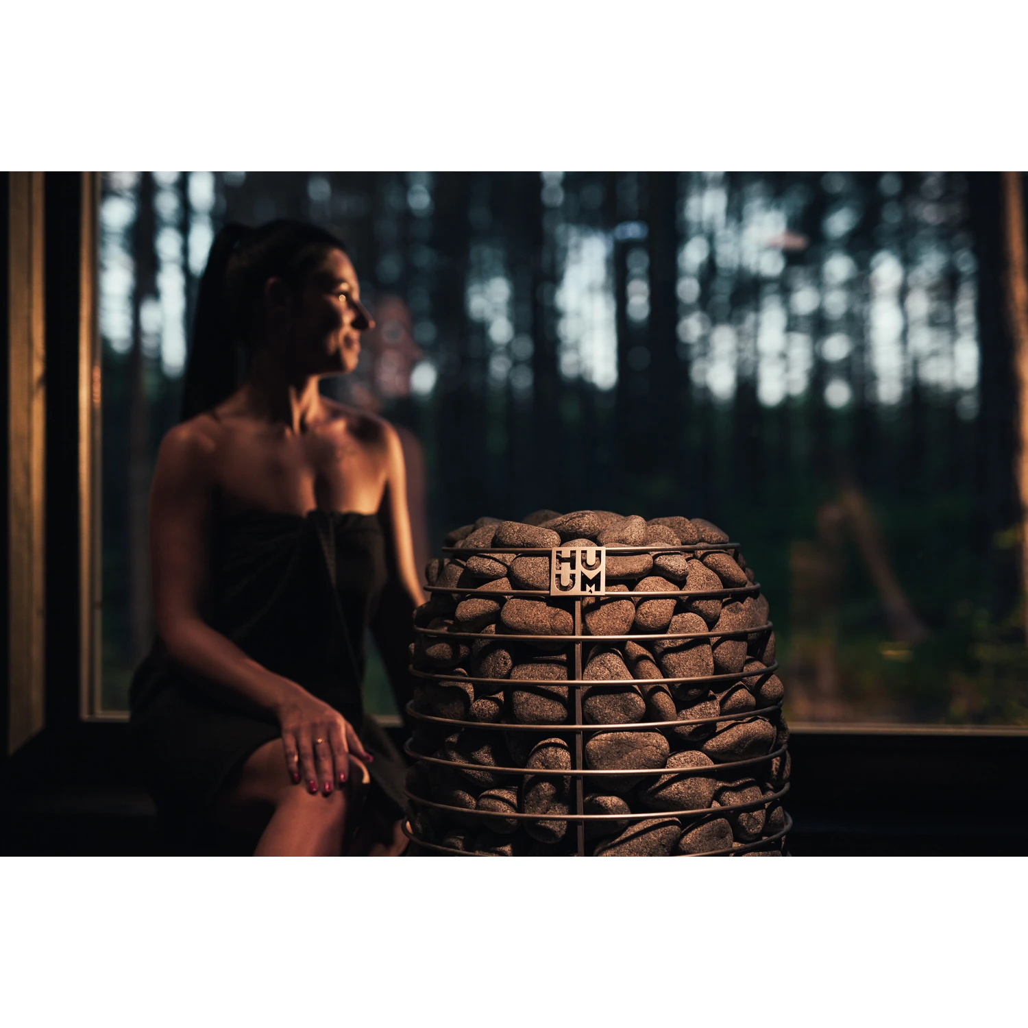 Woman relaxing beside the HUUM HIVE Mini heater in an evening sauna