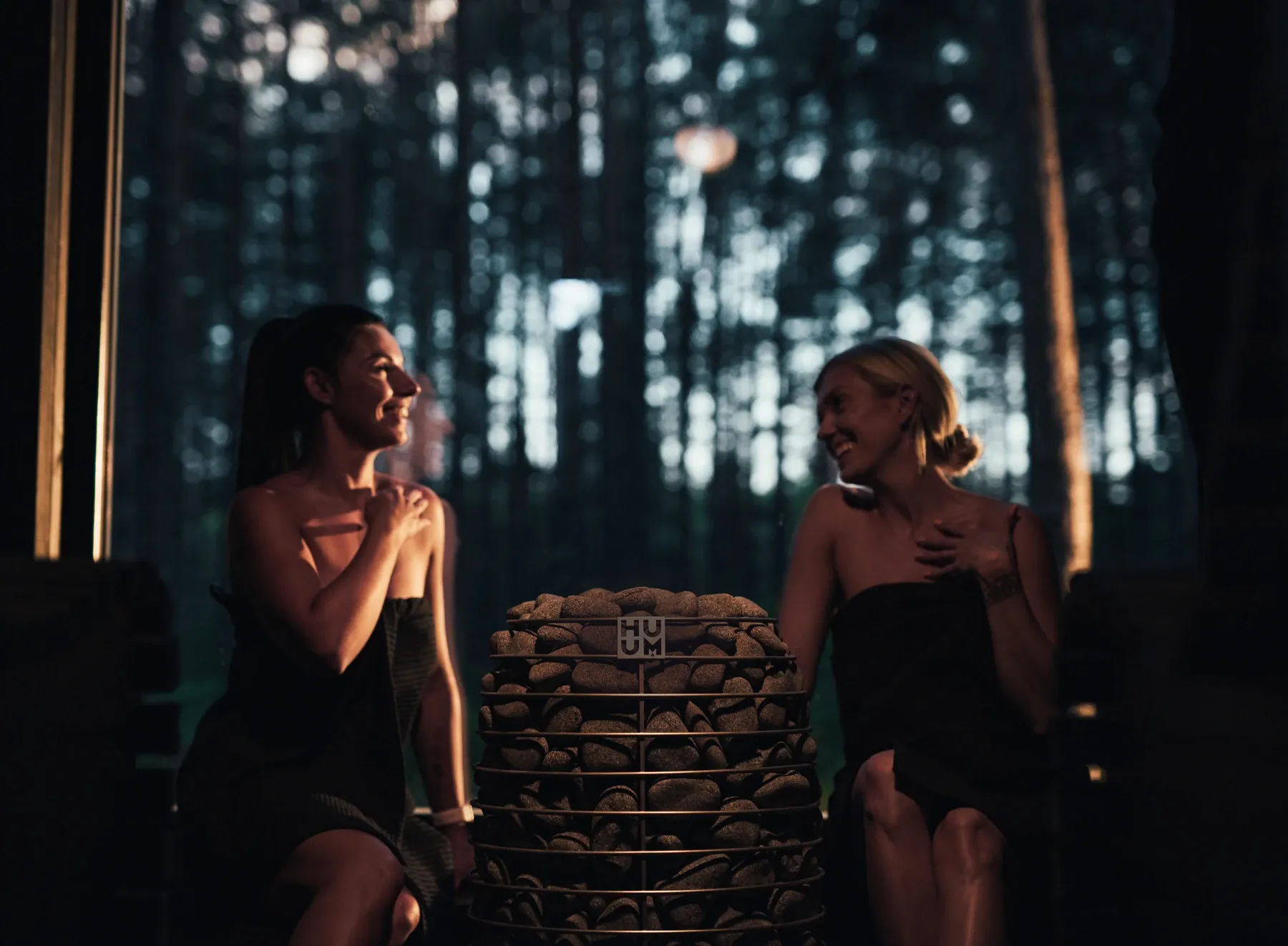 Two friends laughing together in a warm sauna at dusk